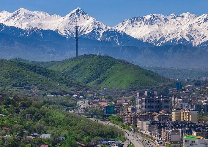 أفق مدينة ألماتي مع جبال تيان شان المغطاة بالثلوج خلف المدينة في ساعة الغروب