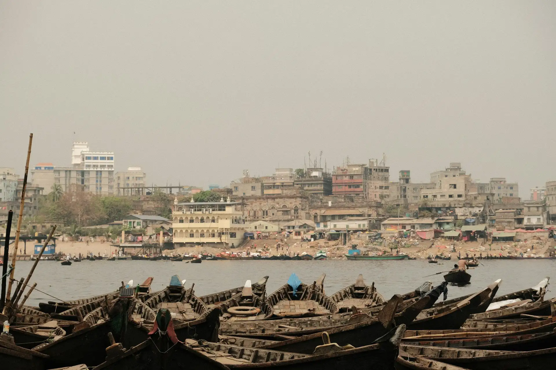 Boats moored on the Buriganga River in Dhaka at golden hour with the old city behind
