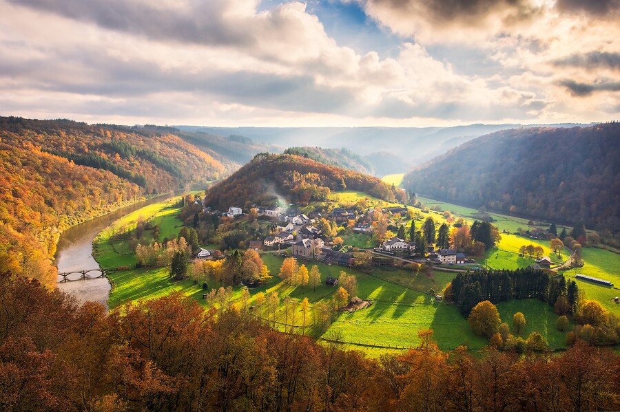 Semois-joen laakso Belgian Ardenneilla syksyllä, metsäiset rinteet oransseina ja kultaisina, sumua veden yllä