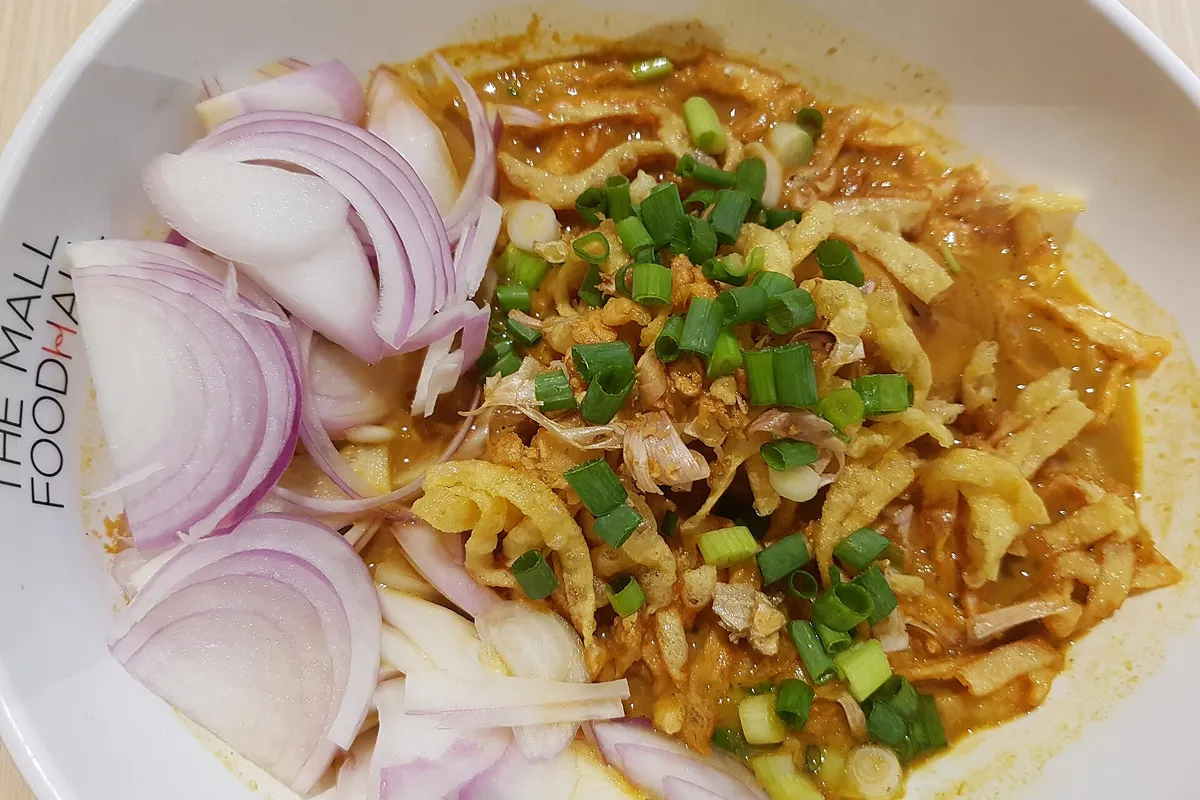 北部タイのココナッツカレー麺スープ、カオソーイの器、揚げ麺、ネギ、エシャロットをトッピング
