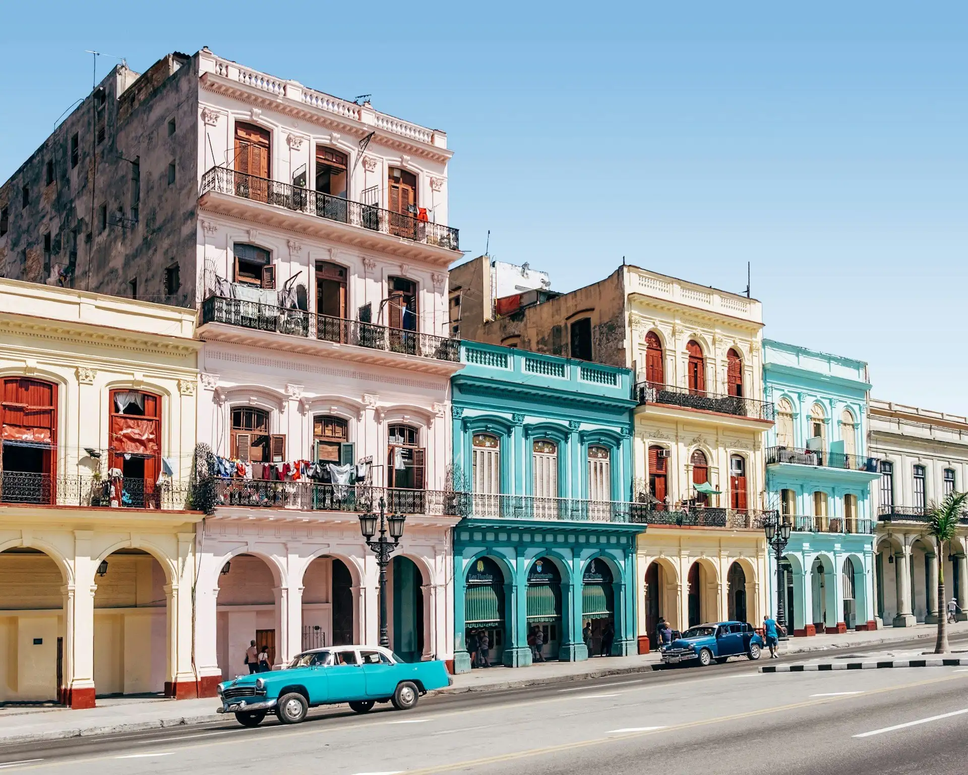 Vintage American cars parked along the Malecón seawall in Havana with crumbling colonial facades and the Caribbean behind them, Cuba