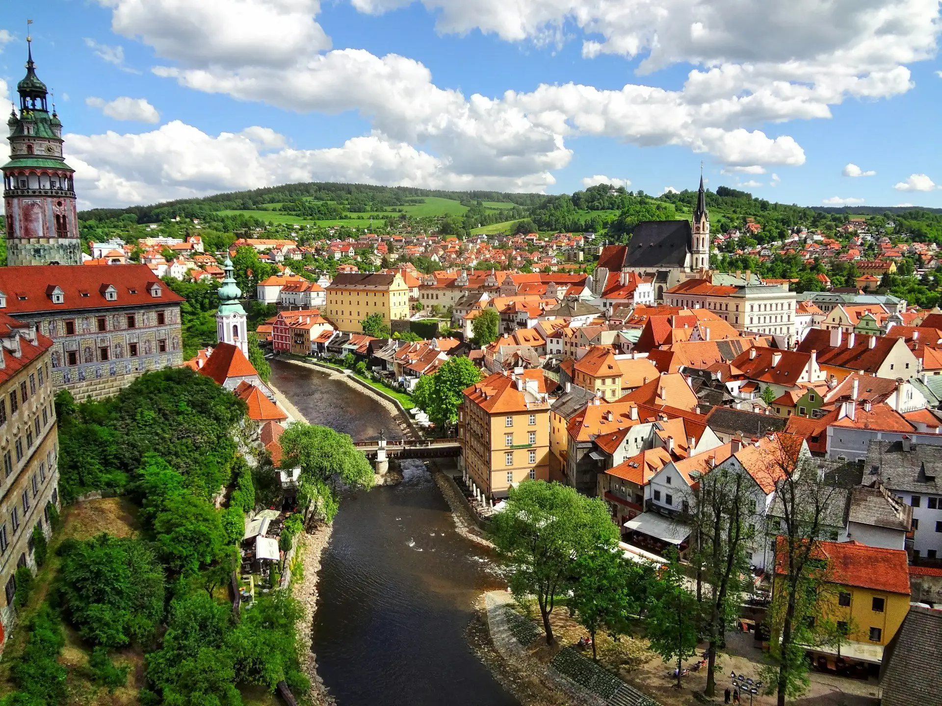 Prague's terracotta rooftops and Gothic spires at dusk seen from above the Old Town, with the Vltava river curving behind the Charles Bridge, Czech Republic