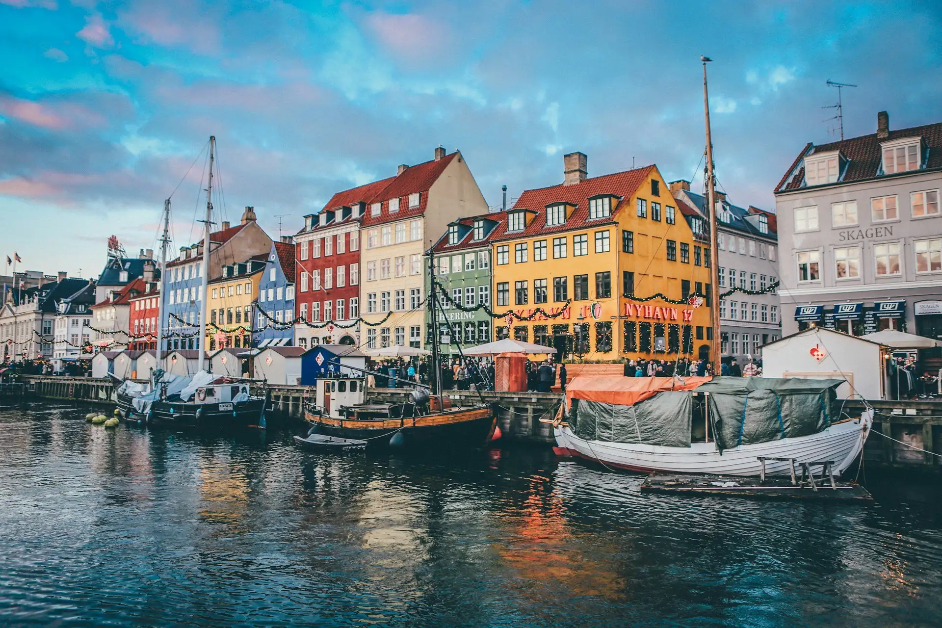 Colourful 17th century merchants' houses lining the Nyhavn canal in Copenhagen on a clear morning with wooden boats moored along the quay, Denmark