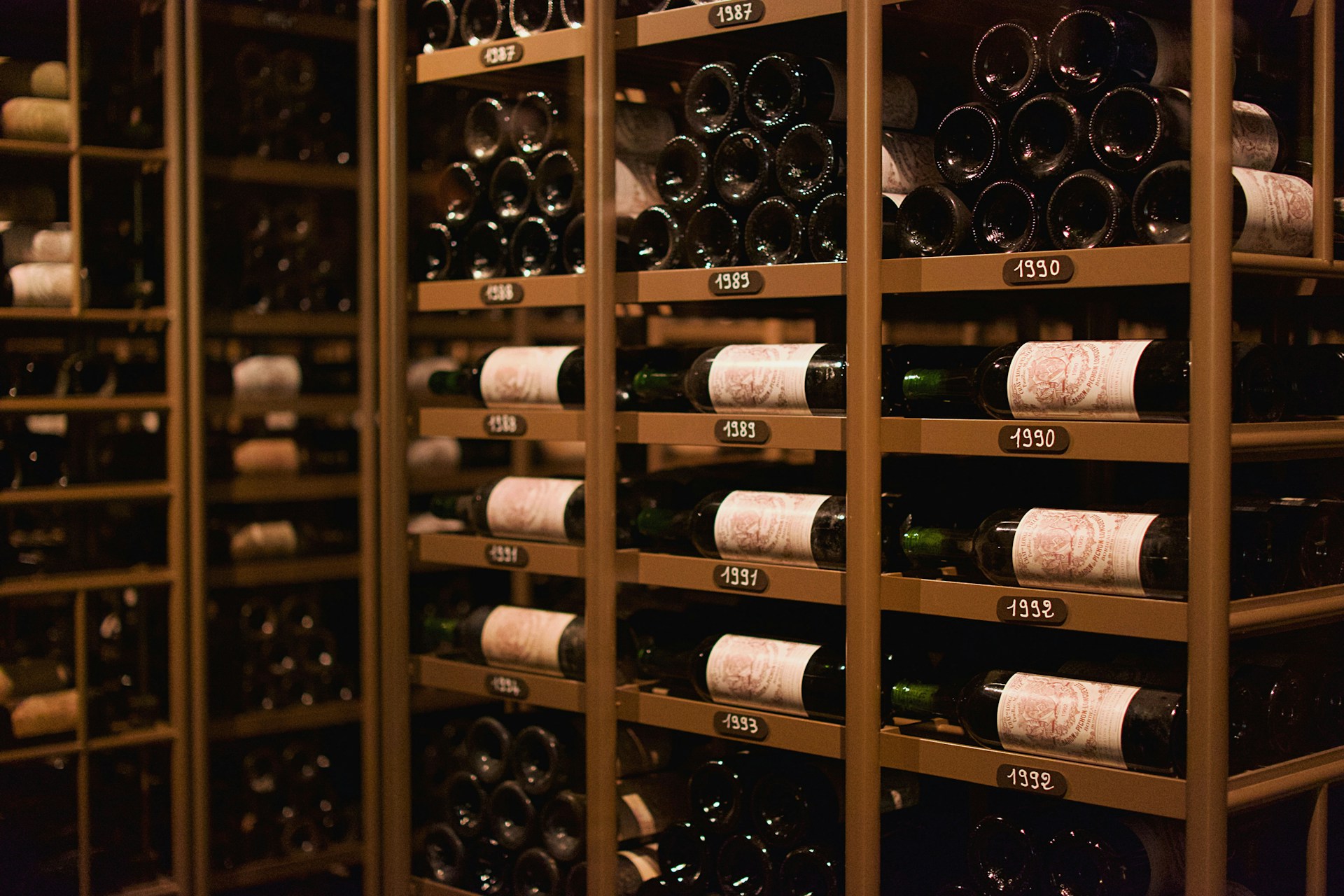 Weingläser mit Bordeaux-Rotwein vor einem französischen Weingut mit Fässern und Steinmauern im Hintergrund