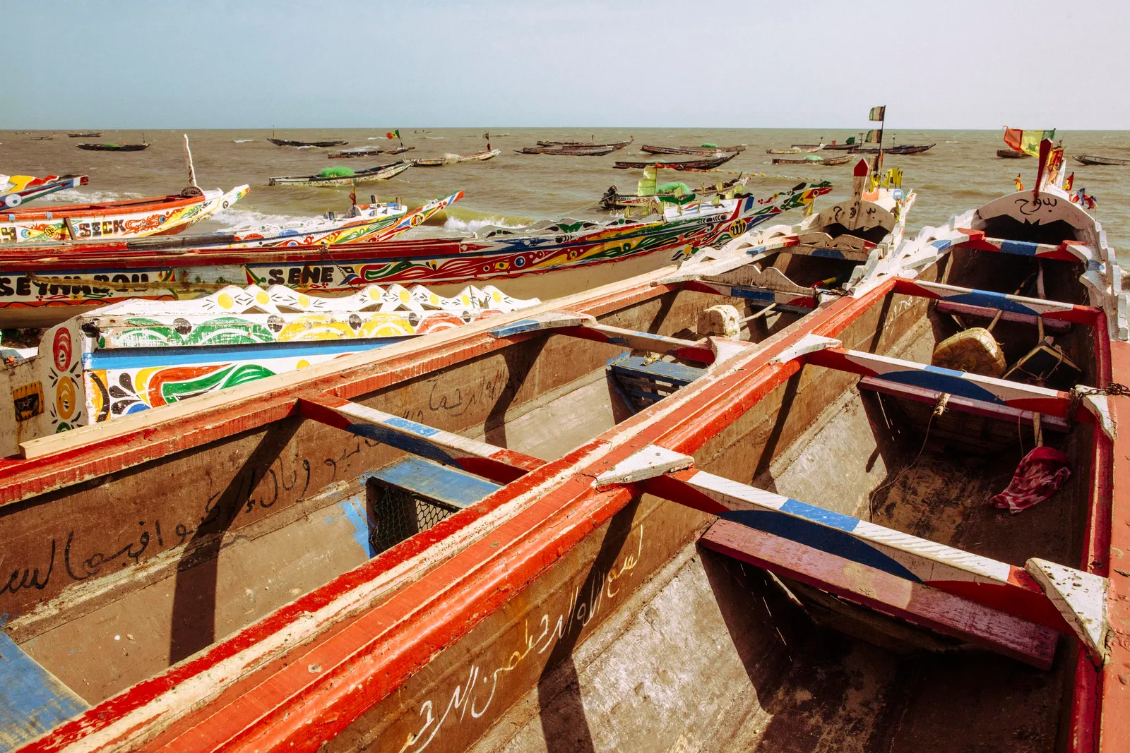 Painted fishing pirogues hauled above the tideline on the Gambia River near Banjul at sunset