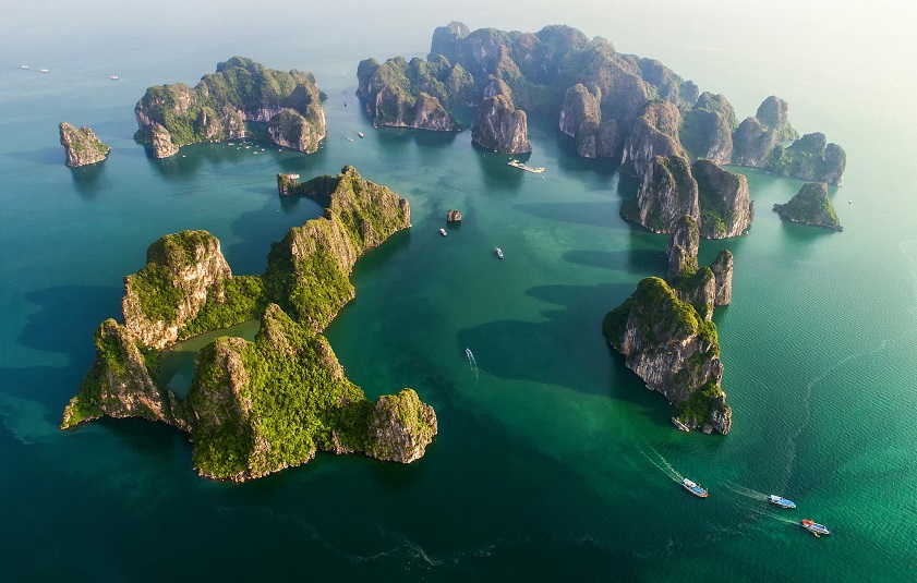Ilhas de carste de calcário e barcos tradicionais de junco na água esmeralda da Baía de Ha Long, Vietname