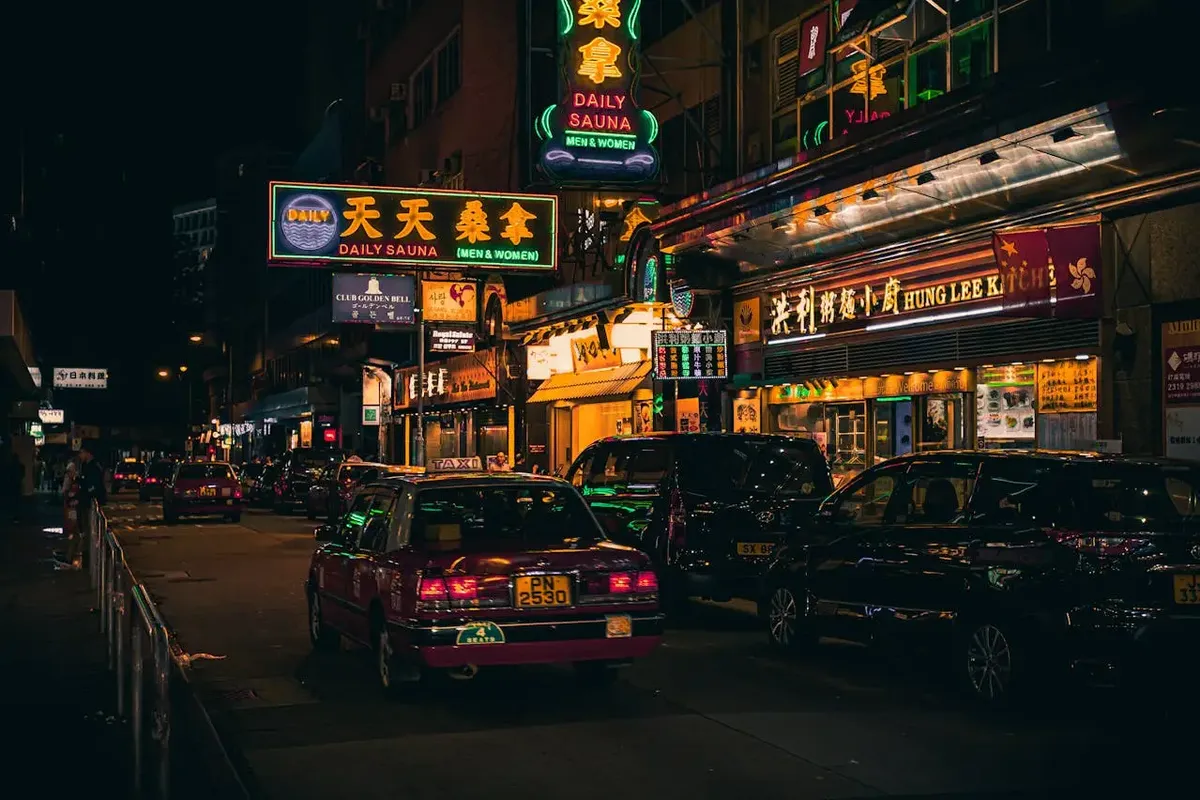 Neonreclames en een rode taxi in een drukke straat in Kowloon bij nacht