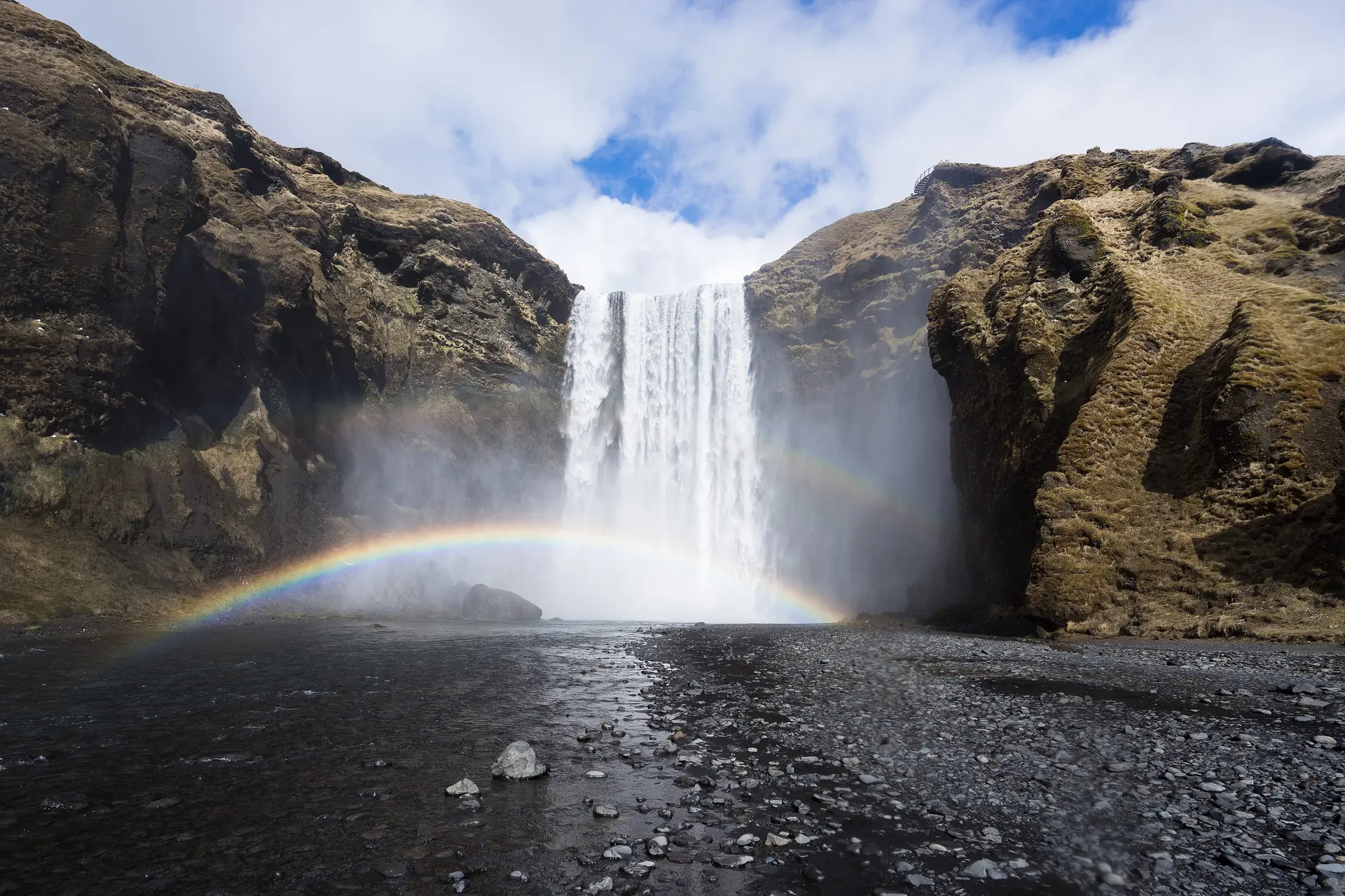 Skógafoss-vesiputous kesällä, sateenkaari vesipilvessä ja vihreät rinteet sen vieressä