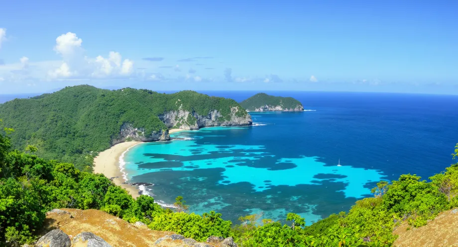 Lombok Tanjung Aan beach with pale sand, clear turquoise water and green hills curving around the bay