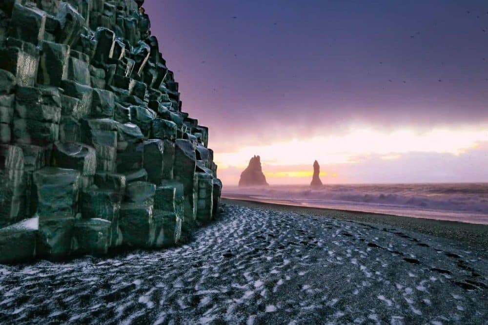 Basaltformaties in zee en zwart zand op het strand van Reynisfjara bij Vik, IJsland