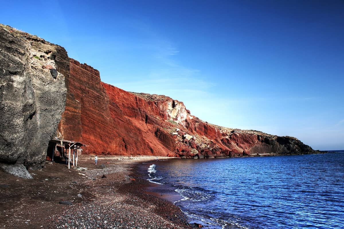 圣托里尼红海滩，陡峭的红色火山悬崖在深色沙滩和清澈蓝色海水上方
