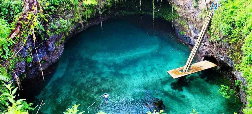 A swimmer descending the wooden ladder into the emerald water of To Sua Ocean Trench, Upolu, Samoa