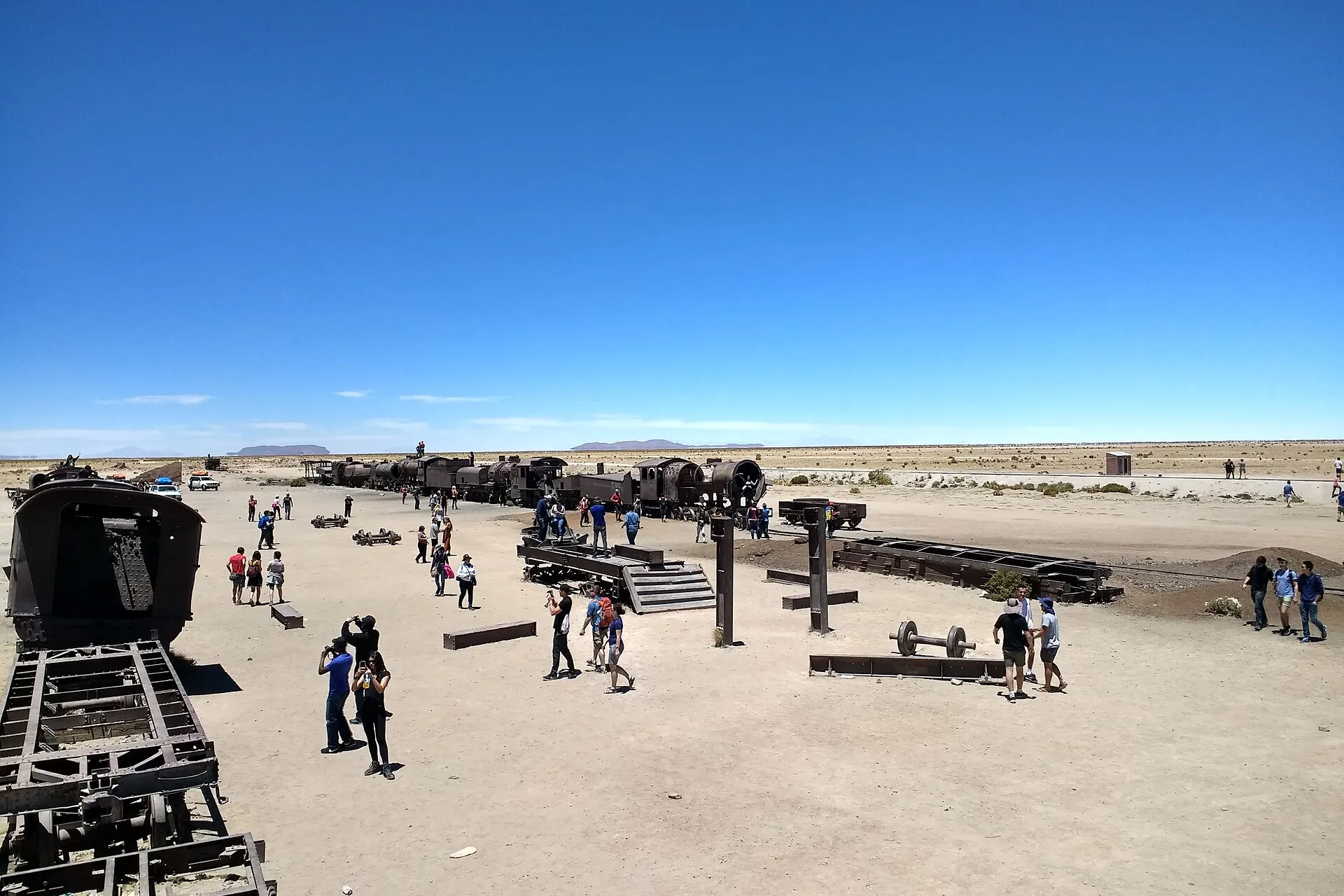 Visiteurs parmi les locomotives à vapeur rouillées du cimetière de trains d'Uyuni sous un ciel bleu profond