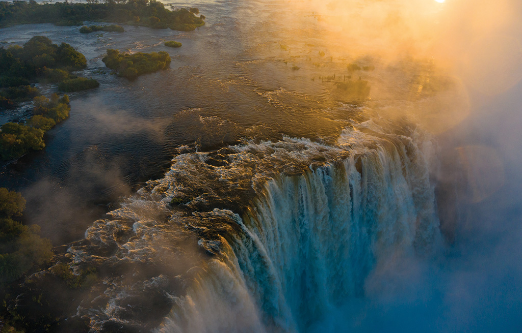 Spray a subir de Victoria Falls no Rio Zambeze, visto do trilho da floresta tropical do Zimbabué à hora dourada